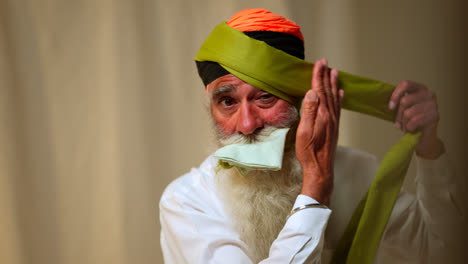 Fotografía-De-Estudio-De-Un-Hombre-Sikh-Mayor-Con-Barba-Atando-Una-Tela-Para-Un-Turbante-Contra-Un-Fondo-Liso,-Filmada-En-Tiempo-Real-2